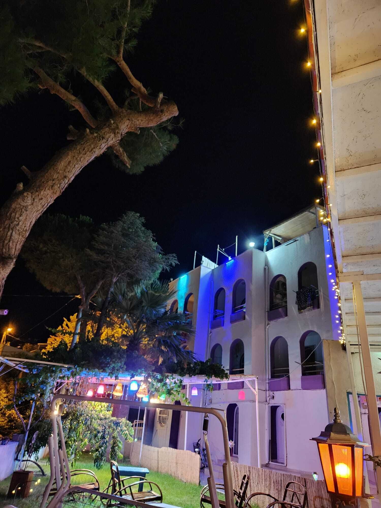 A building with arched windows and a balcony, surrounded by trees and string lights.