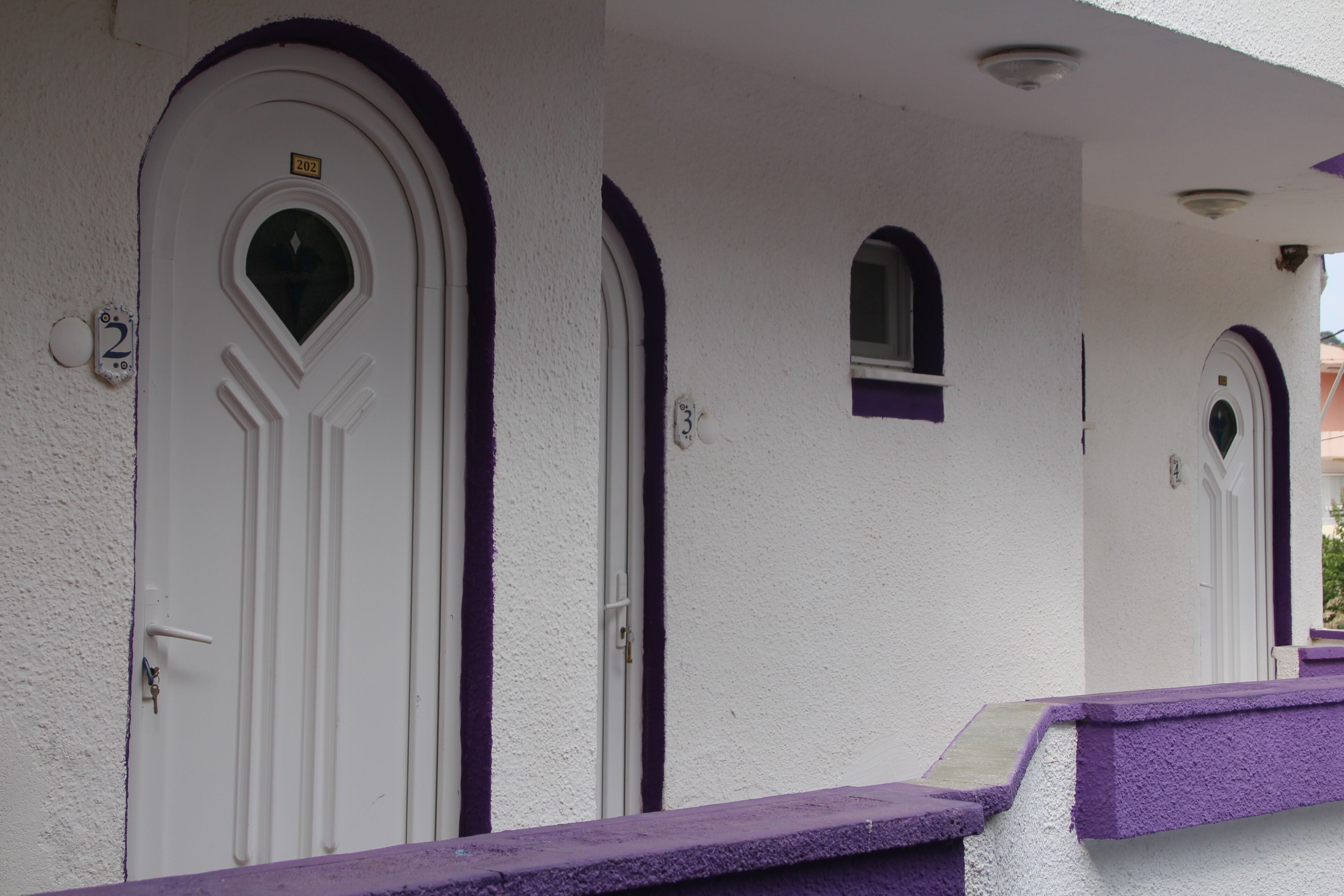 A row of white doors with purple trim and numbers indicating room numbers.