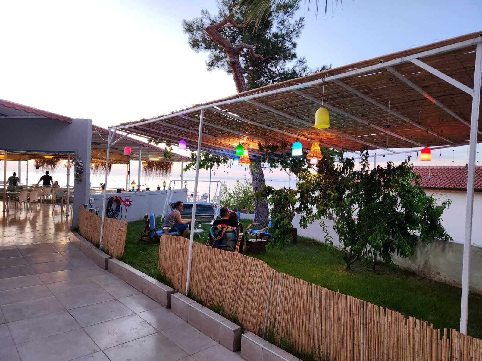 An outdoor seating area with tables and chairs, a covered section with a roof, and a view of the sea.