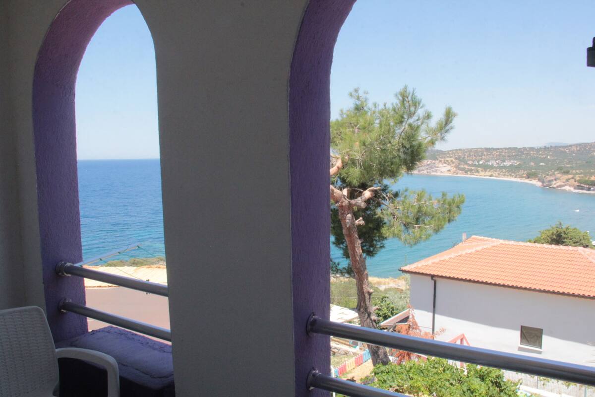 A balcony with a view of the sea and a building with a red roof.