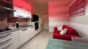 A compact kitchen with white cabinets, a red couch, and a glass table. - Ancora Residence - Downtown Area - Hospital (Piacenza)