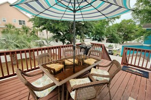 A wooden deck with wicker furniture and a striped umbrella. - Just Beachy | Beautiful Beach Home with Heated Pool (Surfside Beach)