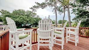 Une terrasse en bois avec des fauteuils Adirondack blancs et une vue sur les arbres et l’océan.