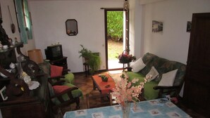 A cozy living room with a green sofa, a wooden coffee table, and a blue tablecloth with nautical prints. There is a potted plant and a hanging light fixture. - Au Calme, Sans vis à vis (Saint-Jean-de-Luz)