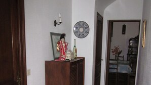A hallway with a wooden door, a cabinet with a decorative item, a wall-mounted plate, and a dining area in the background. - Au Calme, Sans vis à vis (Saint-Jean-de-Luz)