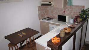A small kitchen with a table, stools, a gas stove, a microwave, and various kitchen items on the counter. - Au Calme, Sans vis à vis (Saint-Jean-de-Luz)