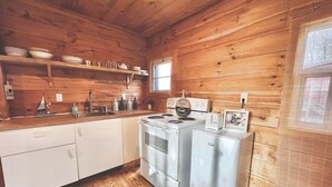 Une cuisine rustique aménagée dans une cabane en bois, avec un poêle, un réfrigérateur et des étagères remplies de vaisselle.