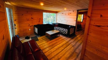A wooden cabin interior with a sofa, a television, and a bench.