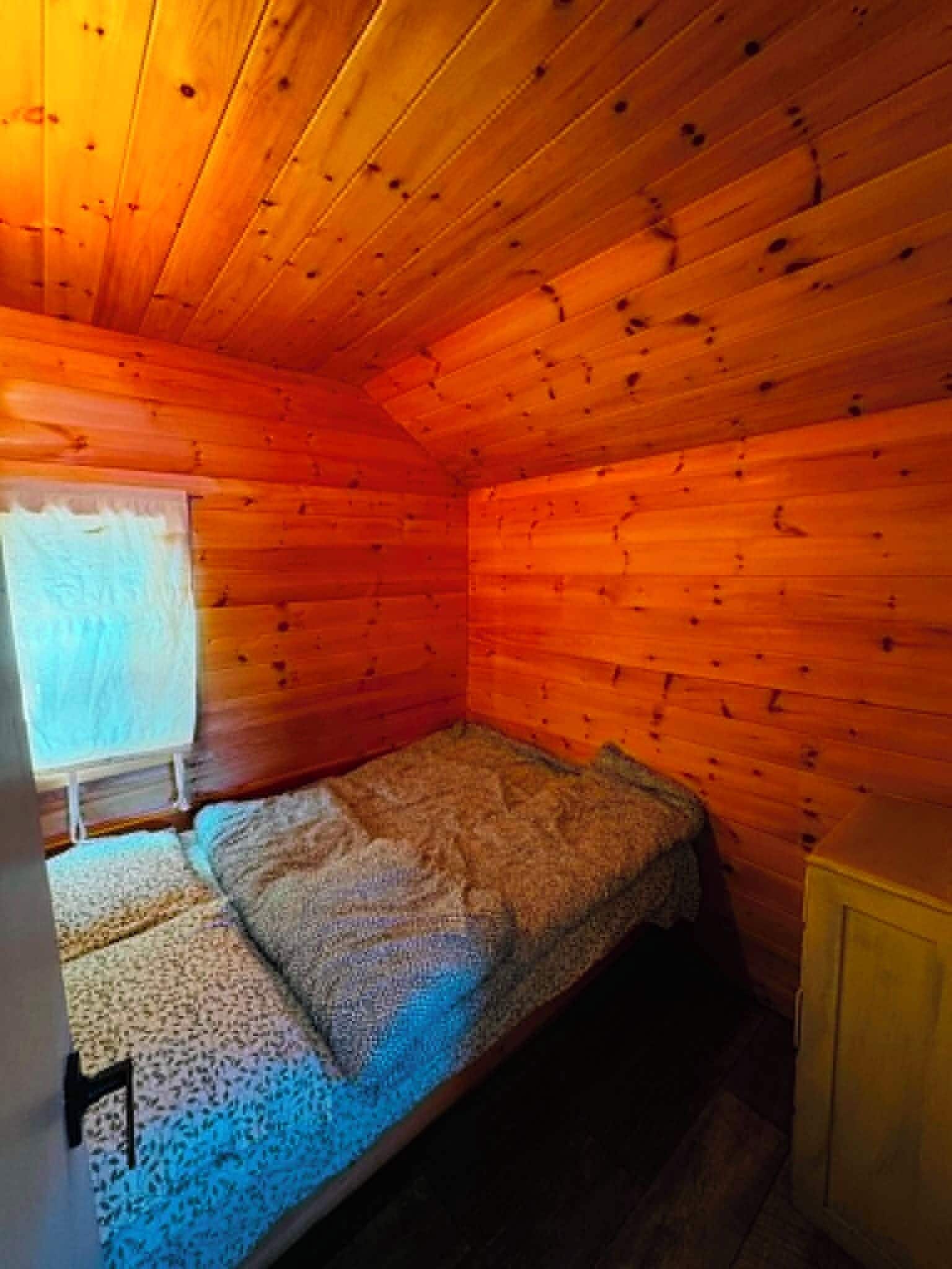 A small, single-bed cabin room with wooden walls and a sloped ceiling.