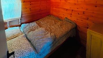 Una piccola camera tipo cabina con un letto singolo, pareti in legno e soffitto spiovente.