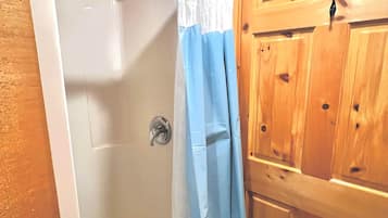 A wooden cabin bathroom with a shower stall, a door with a metal handle, and a wooden cabinet.