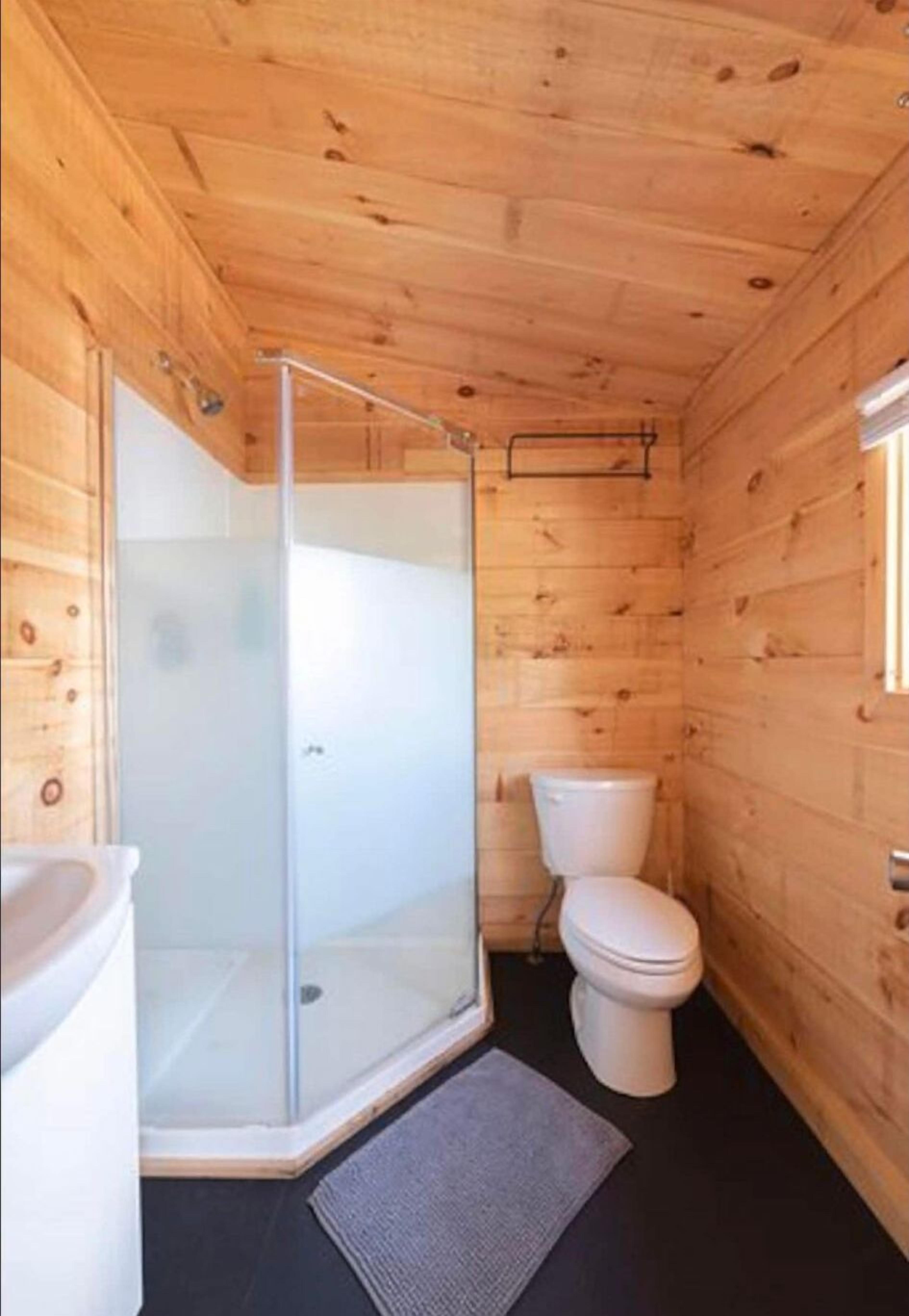 A wooden cabin bathroom with a glass-enclosed shower, a toilet, and a sink.