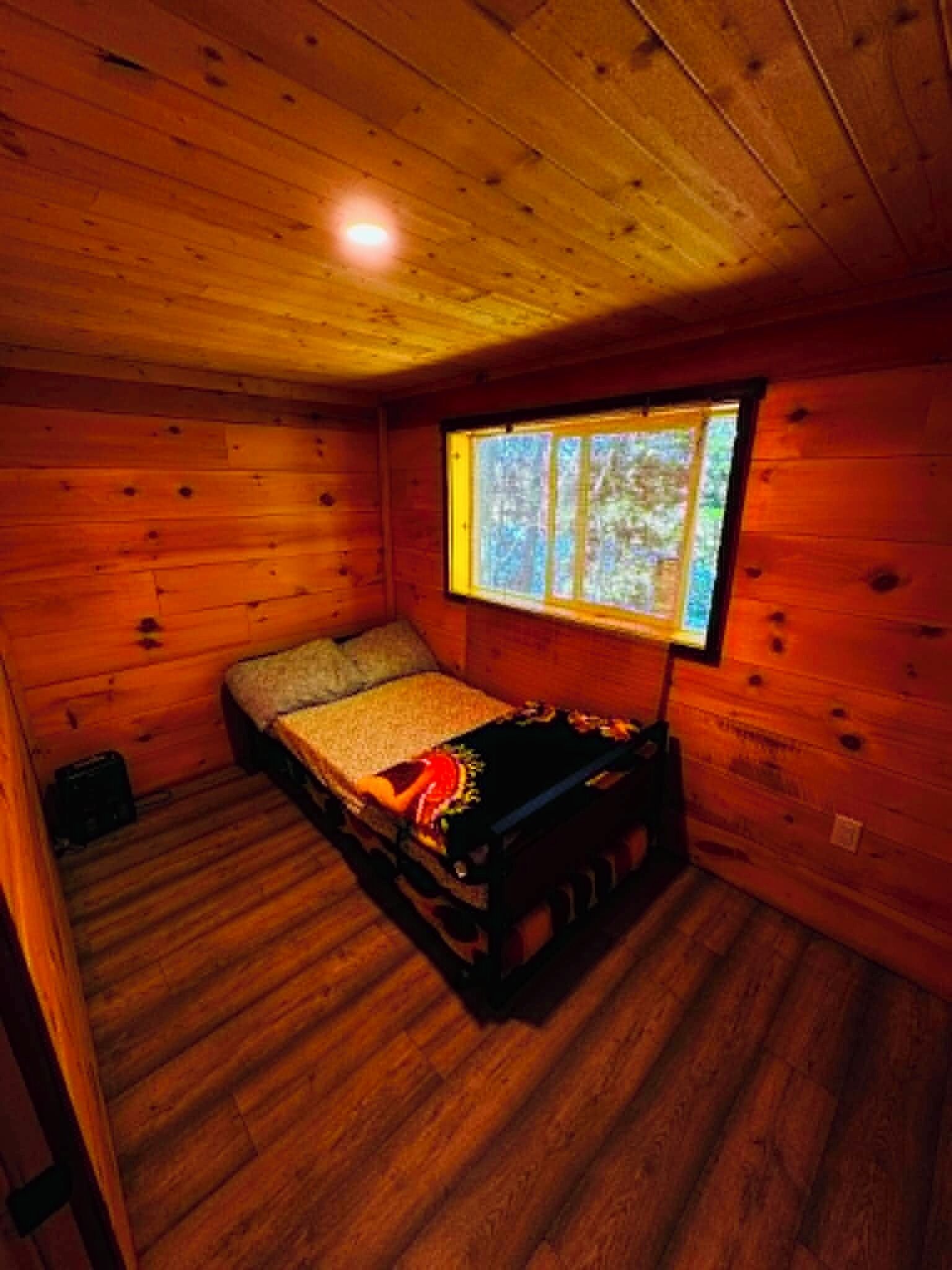 A small cabin room with a single bed, a window, and wooden walls.