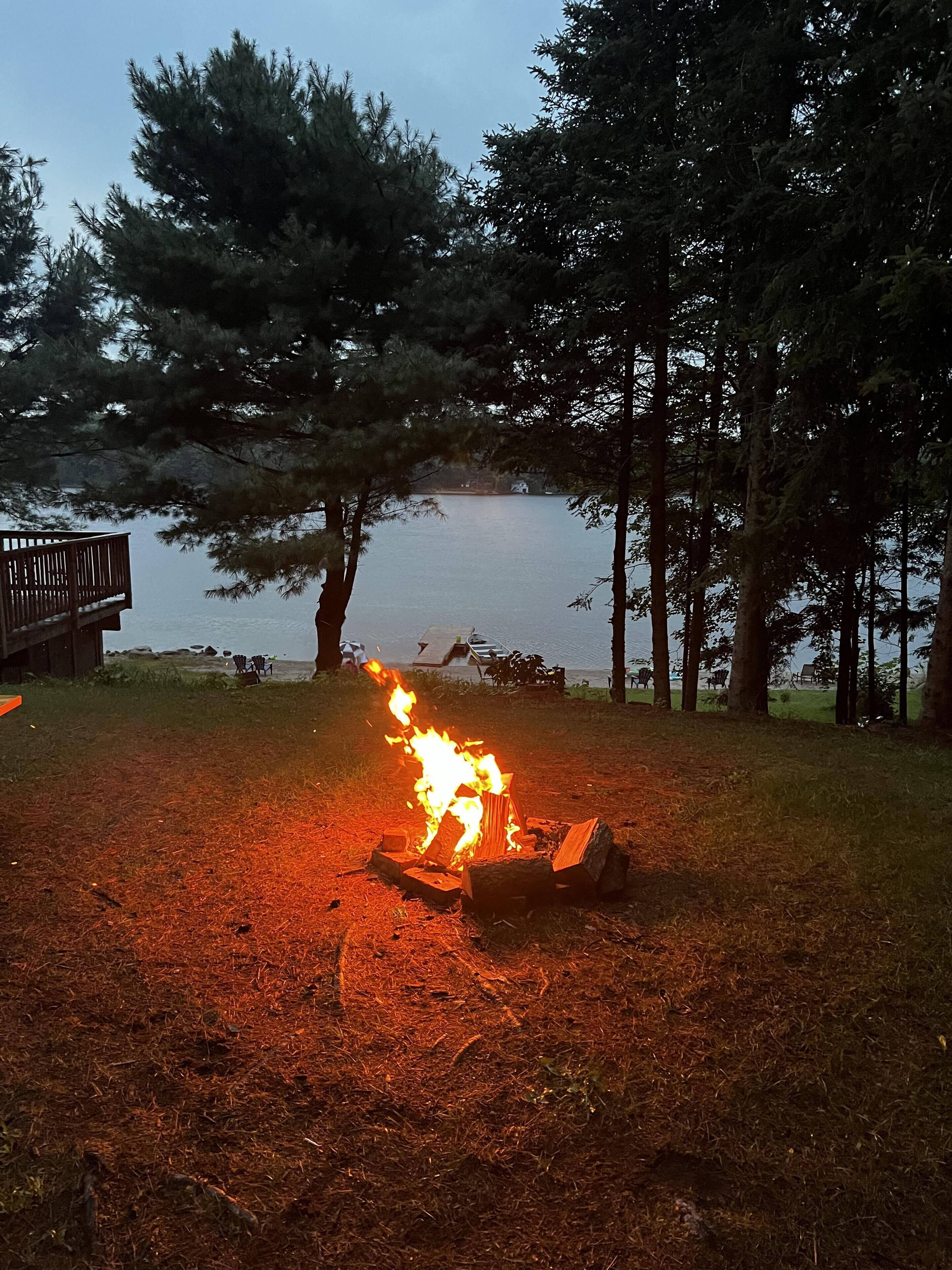 A campfire in a wooded area with a lake in the background.