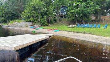 A wooden dock extending into a calm lake, surrounded by lush greenery and a small building with a balcony.