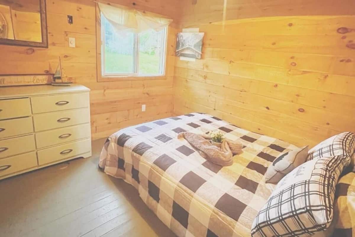 Une chambre dans une cabane en bois, avec un lit, une commode et une fenêtre.