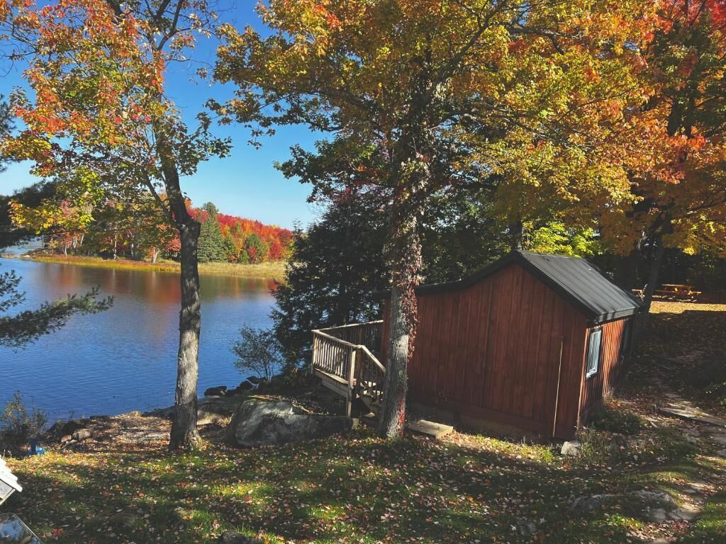 A wooden cabin by a lake with a dock and a staircase leading to a deck.