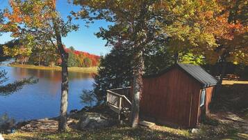 A wooden cabin by a lake with a dock and a staircase leading to a deck.