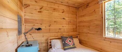 A small wooden cabin room with a bed, a desk, and a window.