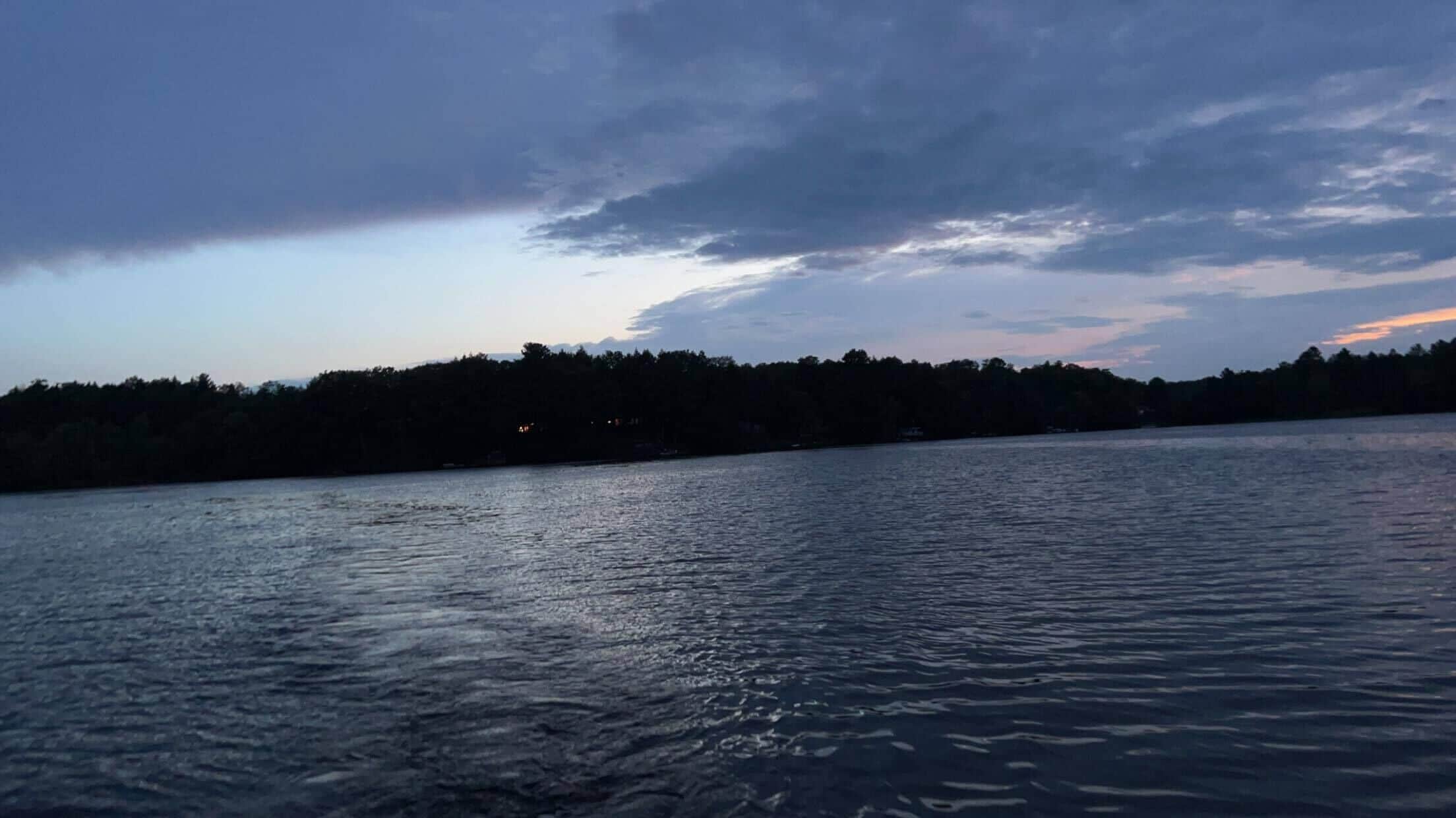 A calm body of water with a forested shoreline and a cloudy sky.