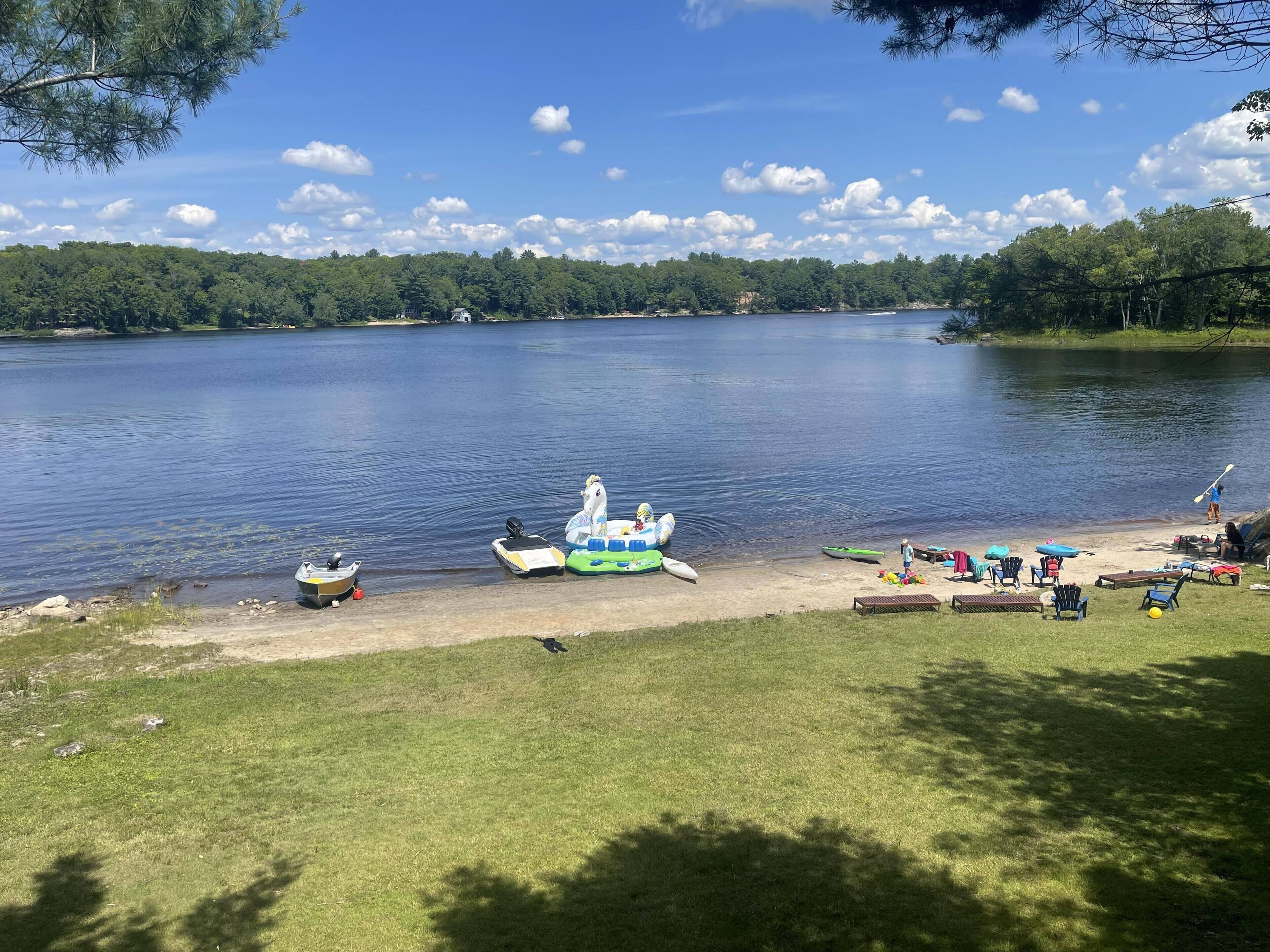 A lakeside setting with inflatable boats, a dock, and a grassy area with chairs and umbrellas.