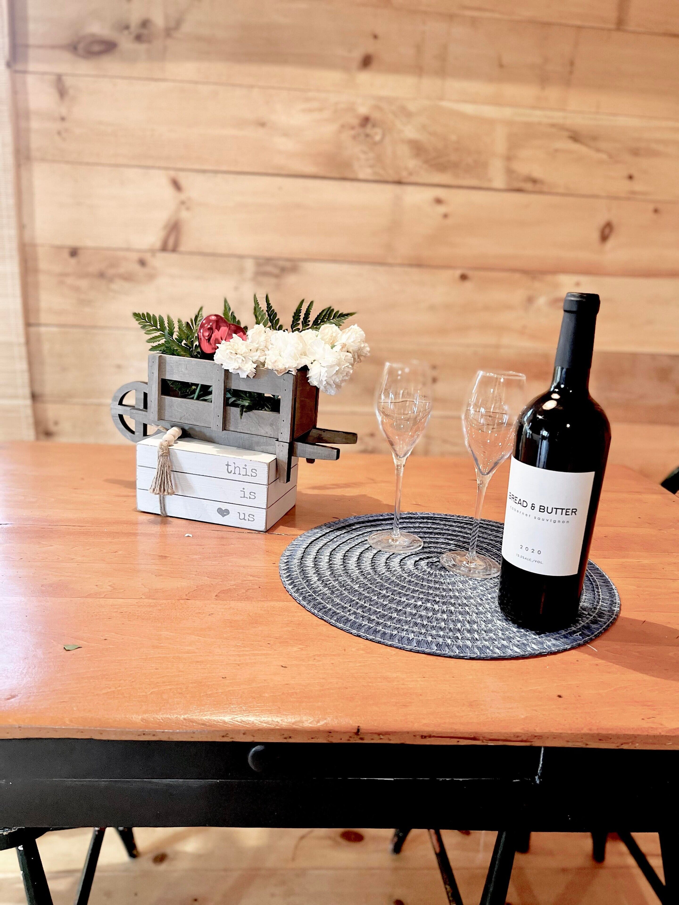 A wooden table with a wine bottle, two glasses, and a decorative box with flowers.