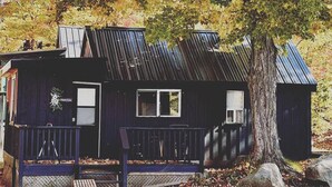 Une cabane rustique avec un toit en métal, une véranda dotée d’un banc et un grand arbre en arrière-plan.