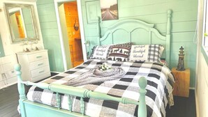 Une chambre à coucher avec une couvre-lit à carreaux, une tête de lit peinte en bleu sarcelle et un miroir au-dessus de la commode.
