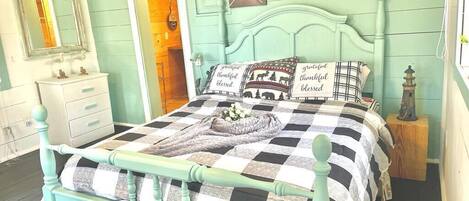 A bedroom with a checkered bedspread, a teal-painted headboard, and a mirror above the dresser.