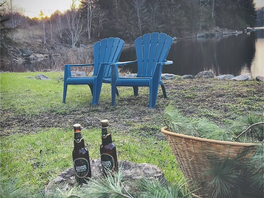 Lammella on kaksi sinistä Adirondack-tuolia, ja niiden lähellä olevalla kivellä on kaksi pulloa Alexander Keith’s -olutta.