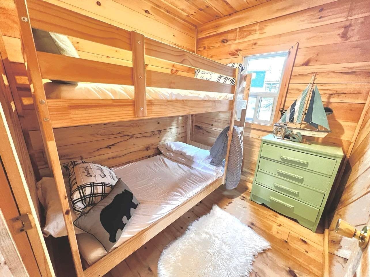 Una habitación tipo cabaña de madera con literas, un aparador verde y una ventana con vistas.
