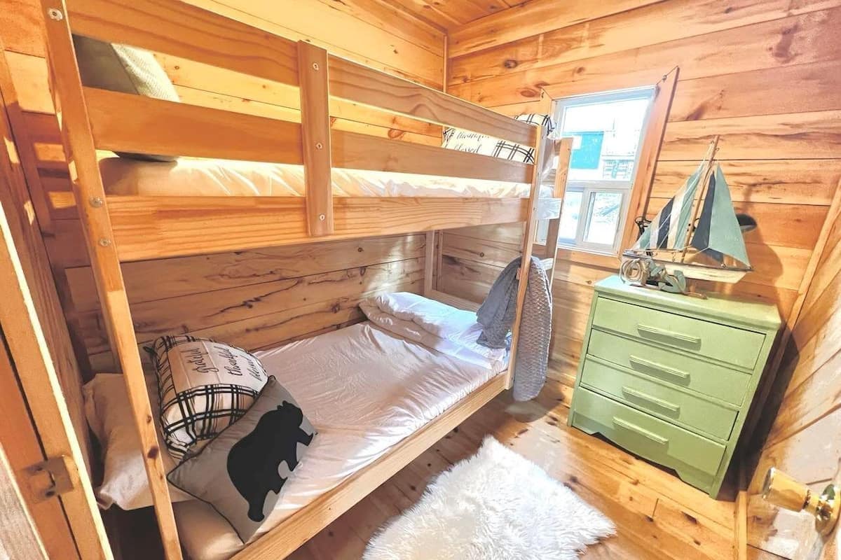 Une chambre dans un chalet en bois, avec un lit superposé, une commode verte et une fenêtre donnant sur un paysage agréable.
