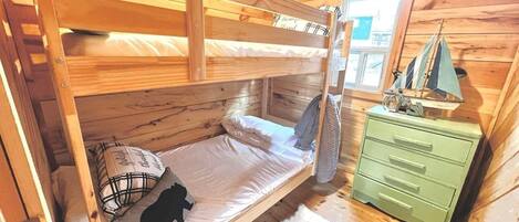 A wooden cabin room with a bunk bed, a green dresser, and a window with a view.