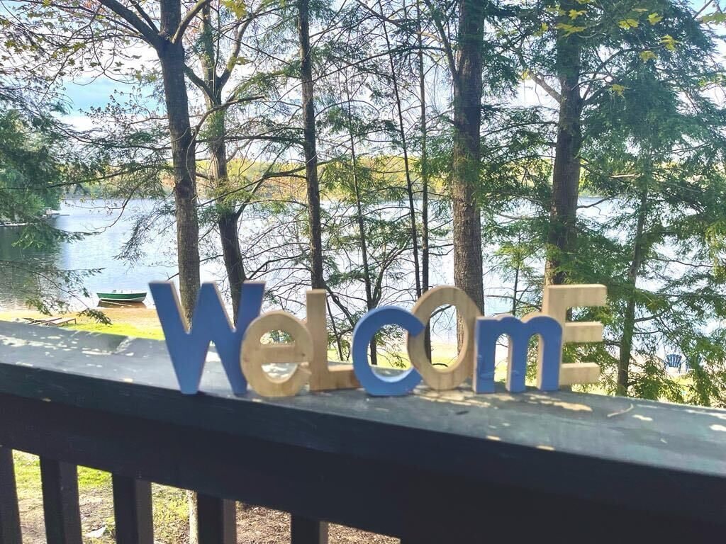 En träveranda med en skylt där det står ”Välkommen”, och med utsikt över en sjö.
