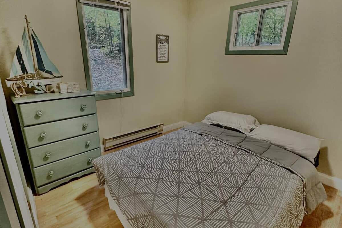Une chambre à coucher comprenant un lit, une commode, deux fenêtres et un ventilateur de plafond.