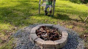 A child sitting on a chair in a backyard with a fire pit in the center.