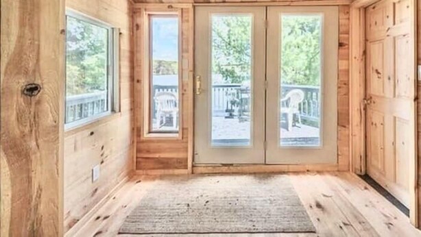 Une cabane en bois dotée d’une grande porte coulissante, d’une petite fenêtre et offrant une vue sur une terrasse et des arbres.