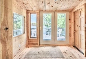 Una cabaña de madera con un amplio ventanal corredera, una ventana pequeña y vistas a una terraza y árboles.