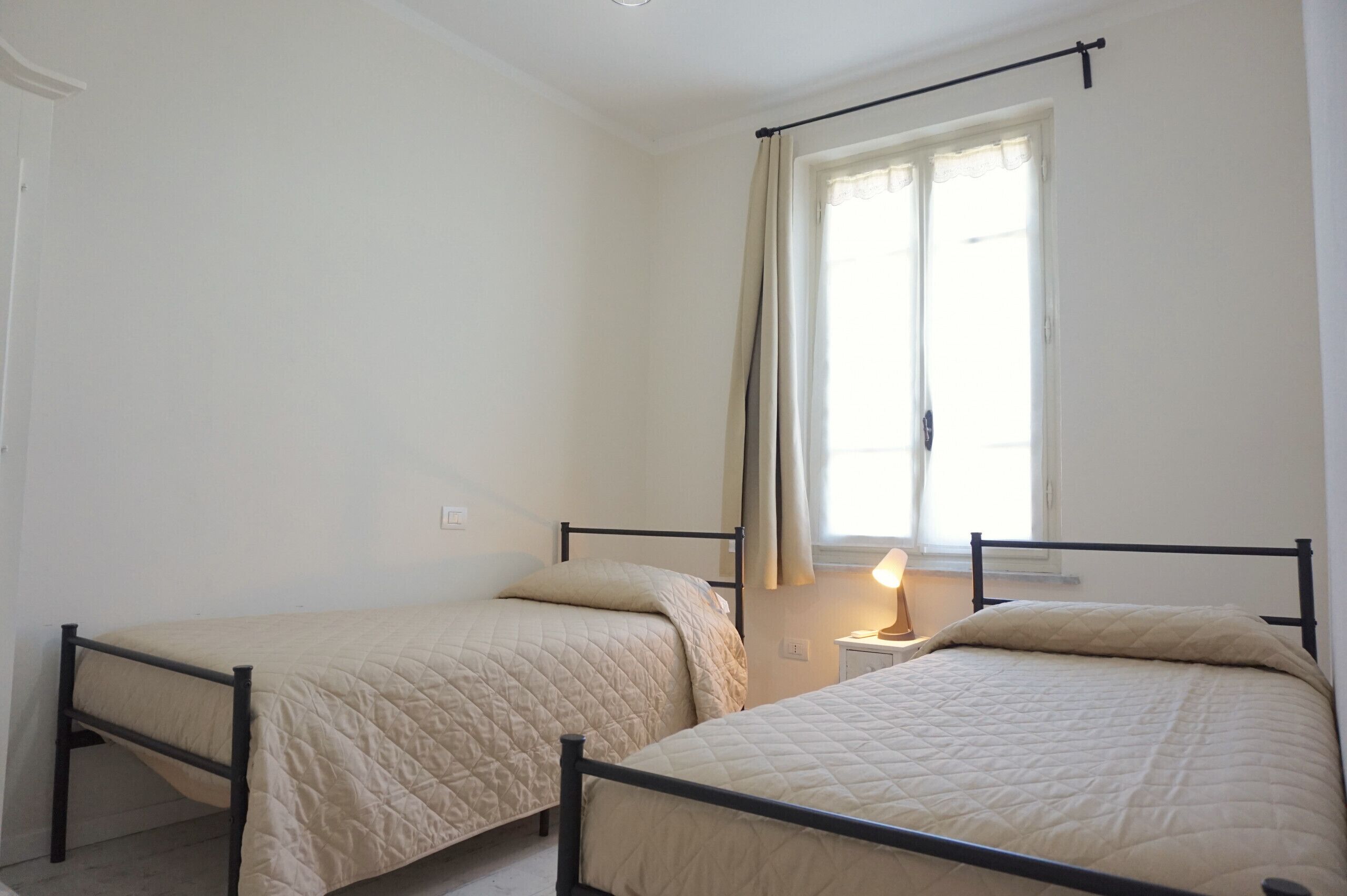 Un dormitorio con dos camas individuales, una ventana con cortinas y una lámpara de noche.