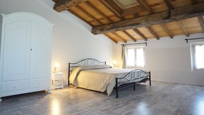 Un dormitorio con techo de madera, una cama con colcha acolchada, un armario blanco y una mesita de noche con lámpara.