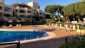 A pool area with lounge chairs and umbrellas, surrounded by a fence and trees.
