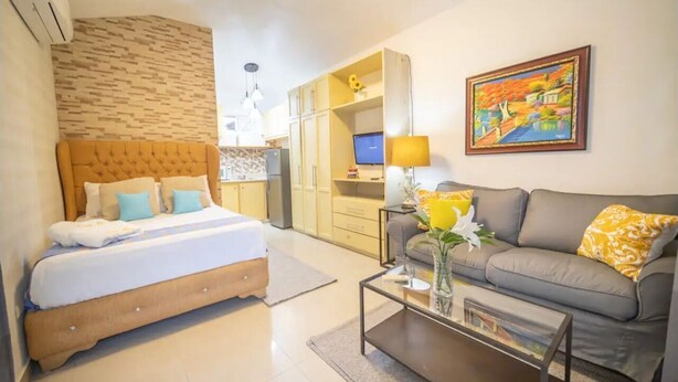 A hotel room with a bed, a sofa, a coffee table, a TV, and a painting on the wall. - Fully Equipped 1BR Studio ->DT->2Mins to the Beach (sosua)