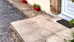 Un edificio con fachada de piedra, contraventanas blancas y una puerta frente a un pequeño jardín.
