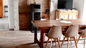 Un comedor con mesa y sillas de madera, chimenea de ladrillo y televisor sobre un mueble de madera.