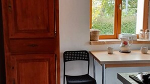 Una cocina con un armario de madera, una silla negra, una ventana con vistas a la vegetación y un suelo de baldosas.