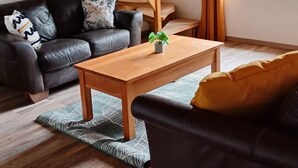 Una sala de estar moderna con una escalera de madera, un sofá de cuero negro, una mesa de centro de madera y un ventanal con cortinas.