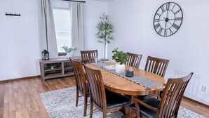 A dining area with a wooden table, six chairs, a clock on the wall, and a potted plant.