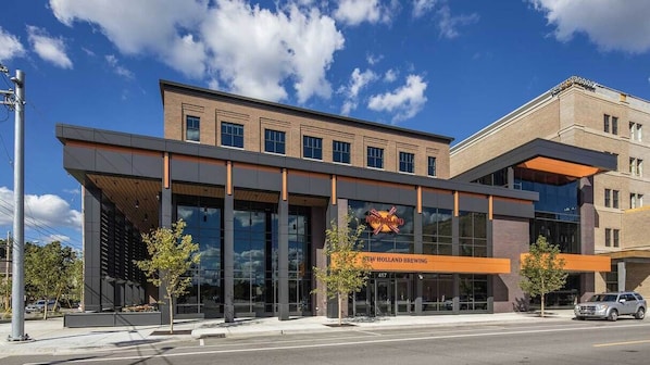 A modern building with a glass facade, a prominent sign for New Holland Brewing, and a clear sky.