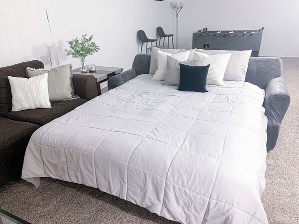 A neatly arranged bedroom with a large bed, a sofa, a small table with a plant, and a futsal table. - Beckwith Bungalow - Mins from Downtown & Local Favorites, Updated, Modern (Grand Rapids)