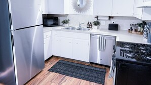 A modern kitchen with white cabinets, stainless steel appliances, a microwave, a sink, a toaster, and a gas stove.